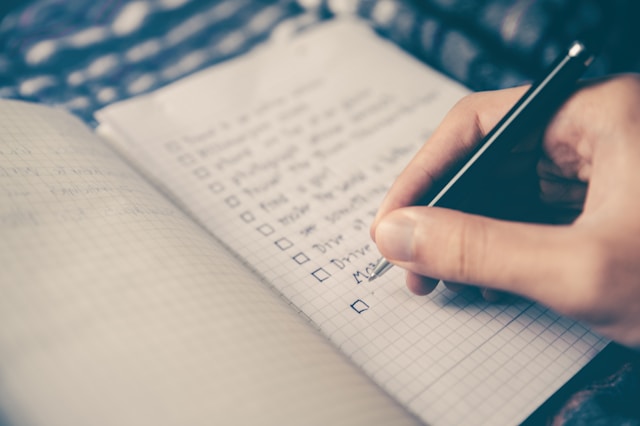 A hand writing a to-do list on a notebook by Glenn Carstens.