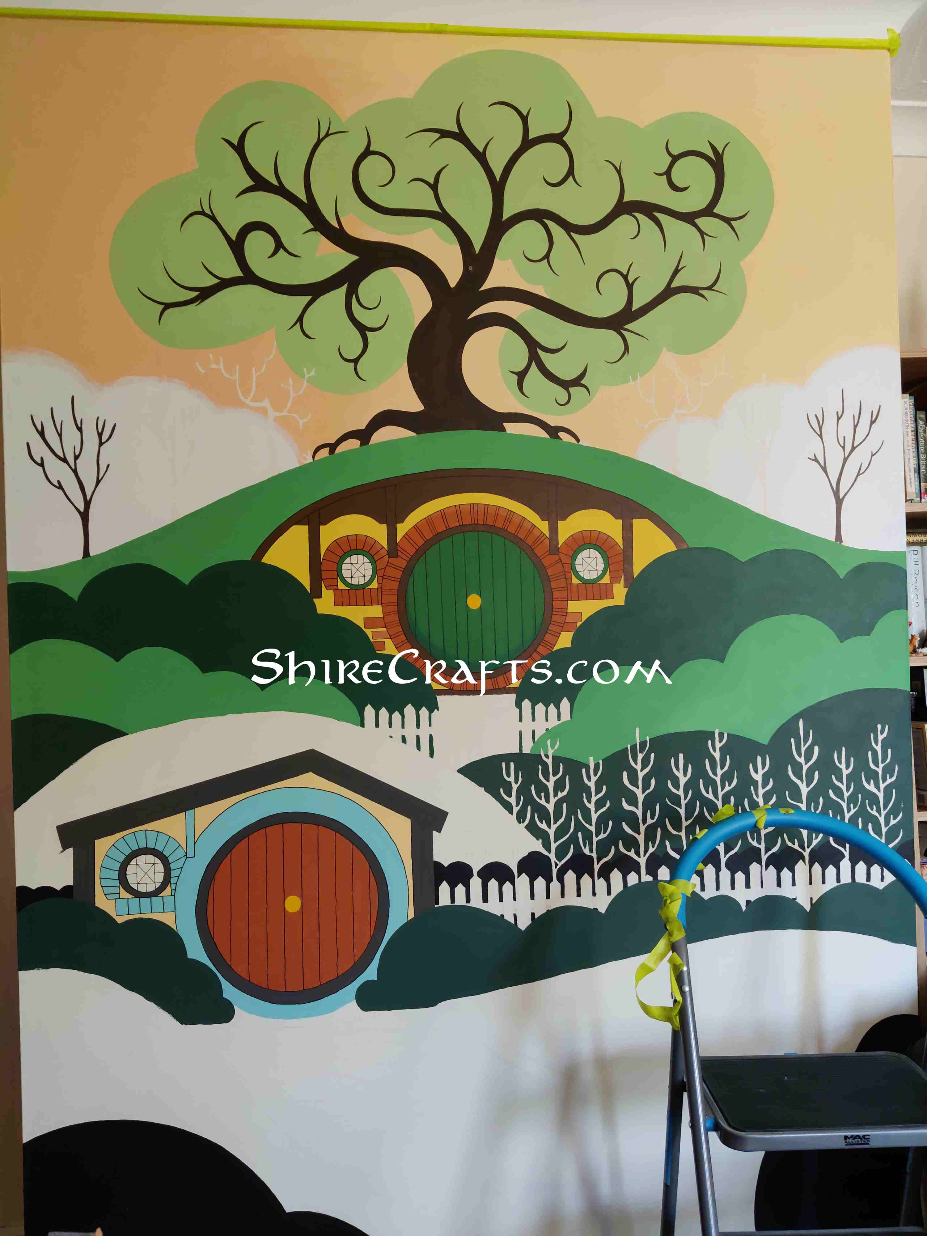 Picture of a wall with an image of the shire being painted on it, some more colors have been added