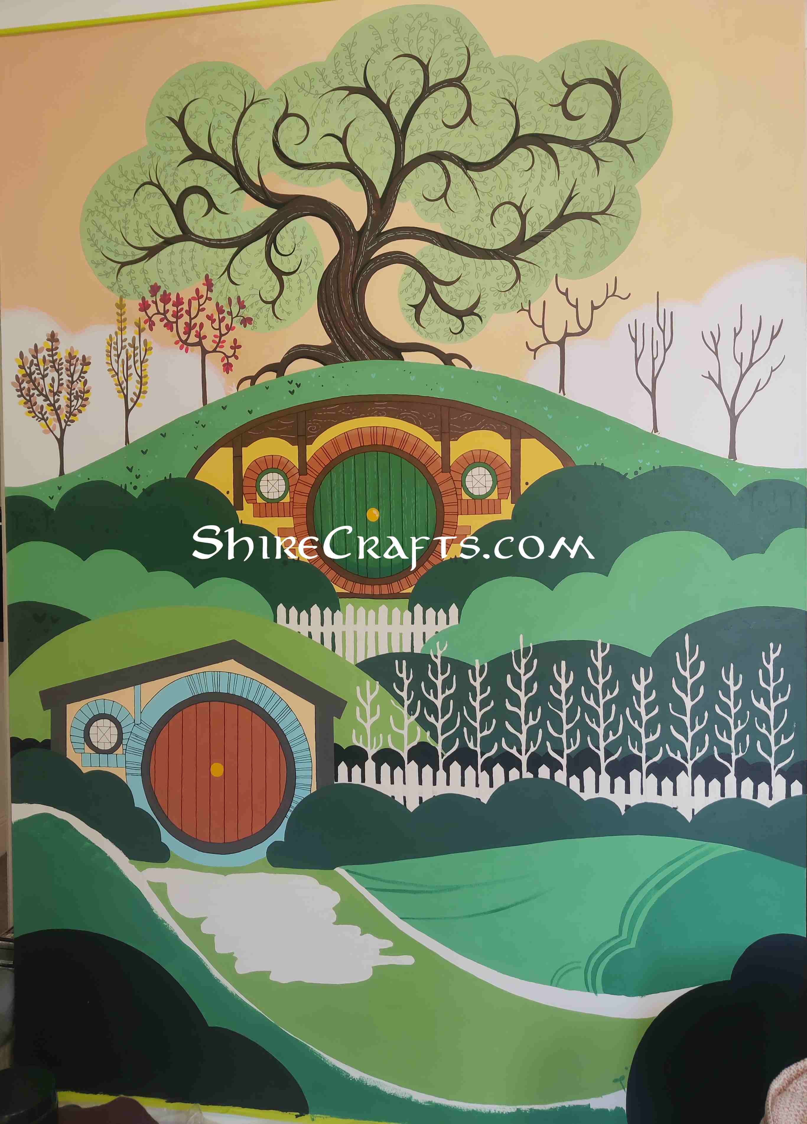 Picture of a wall with an image of the shire being painted on it, almost all the base colors and some details have been painted