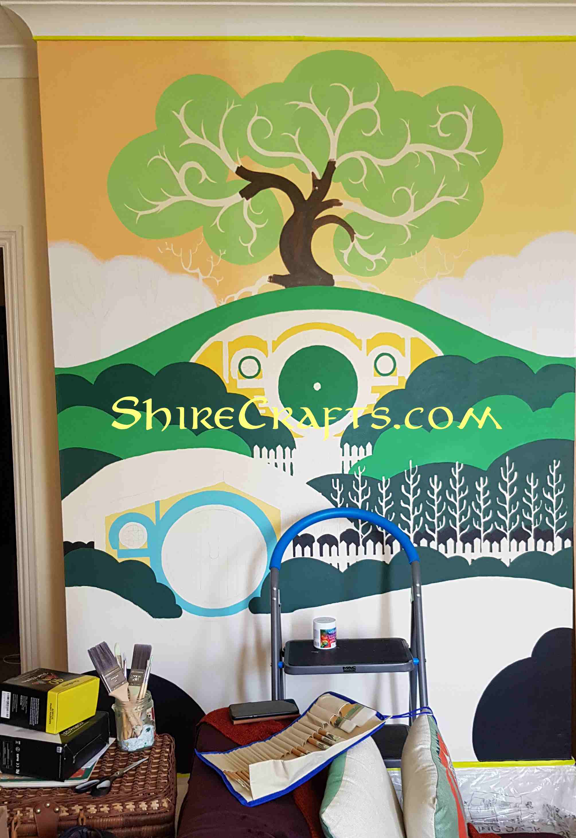 Picture of a wall with an image of the shire being painted on it, only some base colors are present
